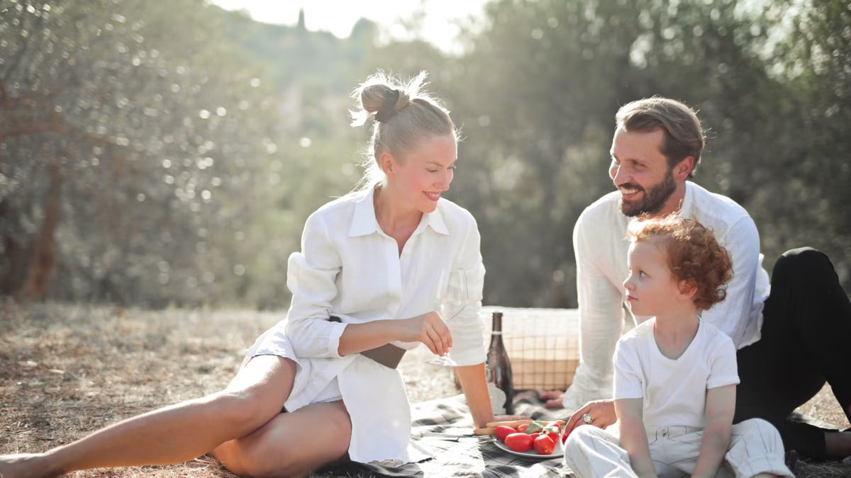A cheerful family enjoying a picnic outdoors with smiles and sunny skies.